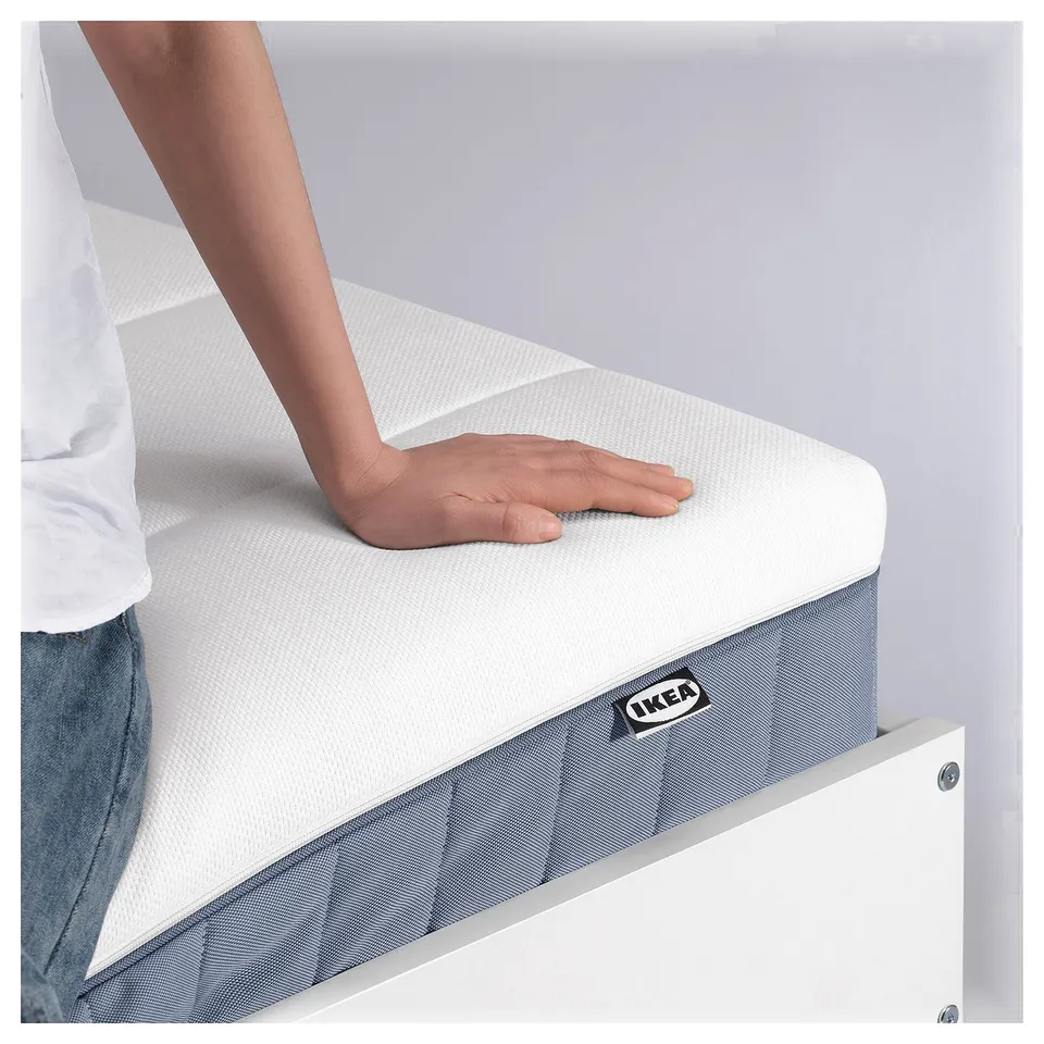 A person demonstrating IKEAs firm white VALLBERGET mattress, showcasing its firm support and natural materials.