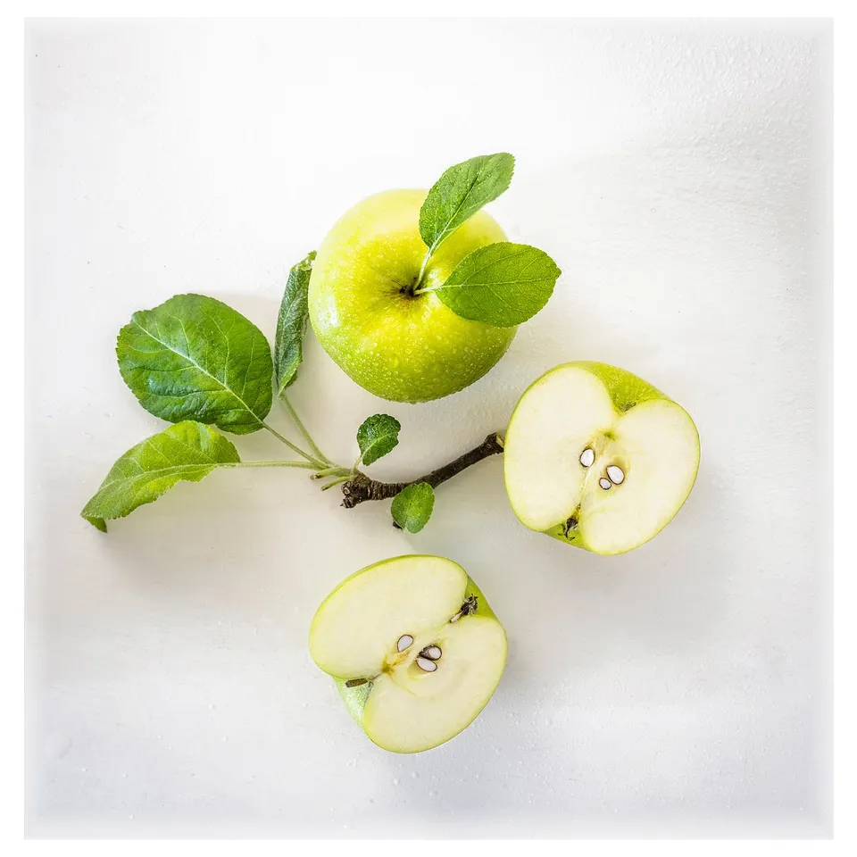 Fresh green apples and leaves on white surface.