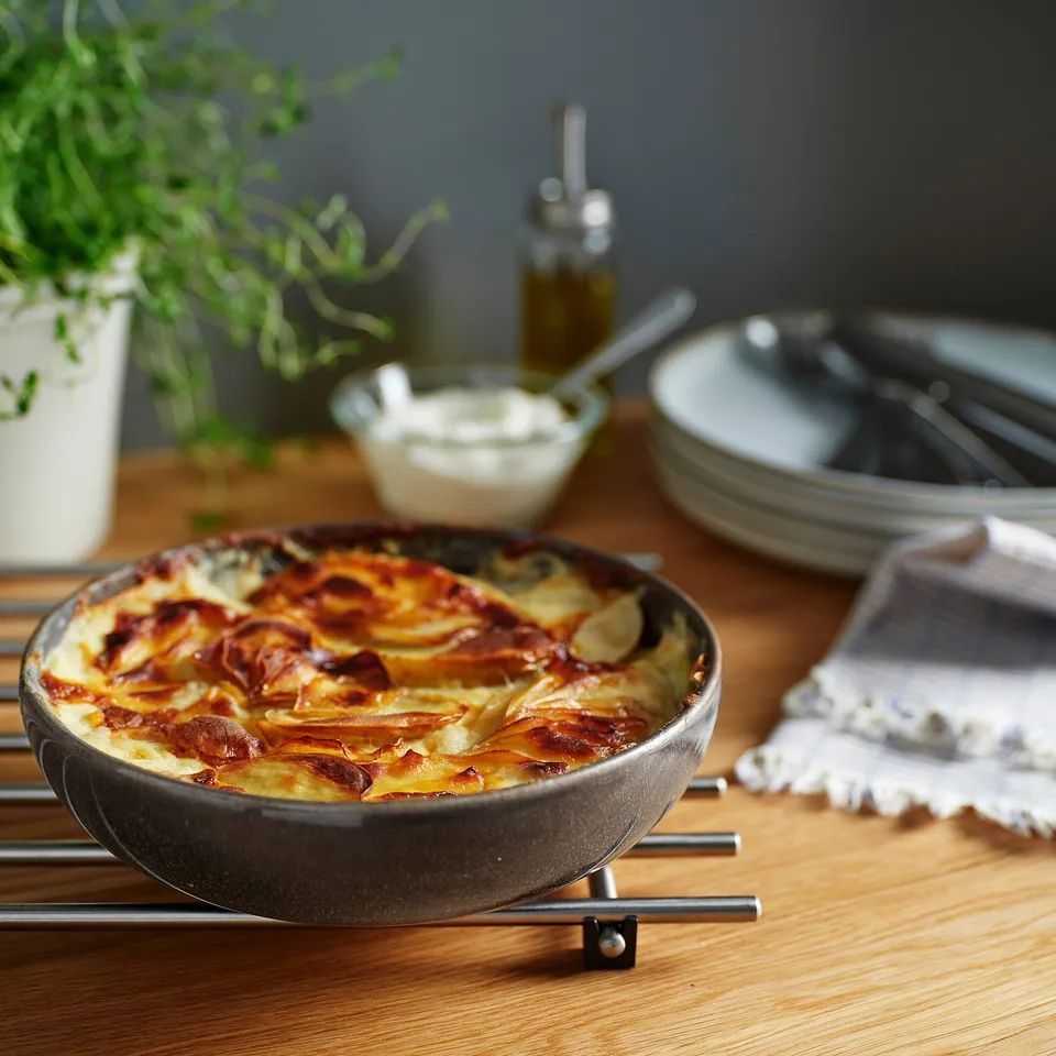 GLADELIG dark-grey oven dish, small and deep, stoneware, holds a large serving, surrounded by plates, cutlery, and plant.