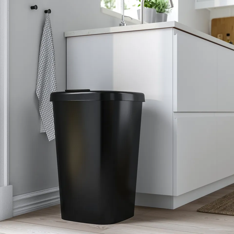 Black LÖVKVAST bin next to white cabinets. Tall, slim, polypropylene, waste sorter with lid and bag openings.