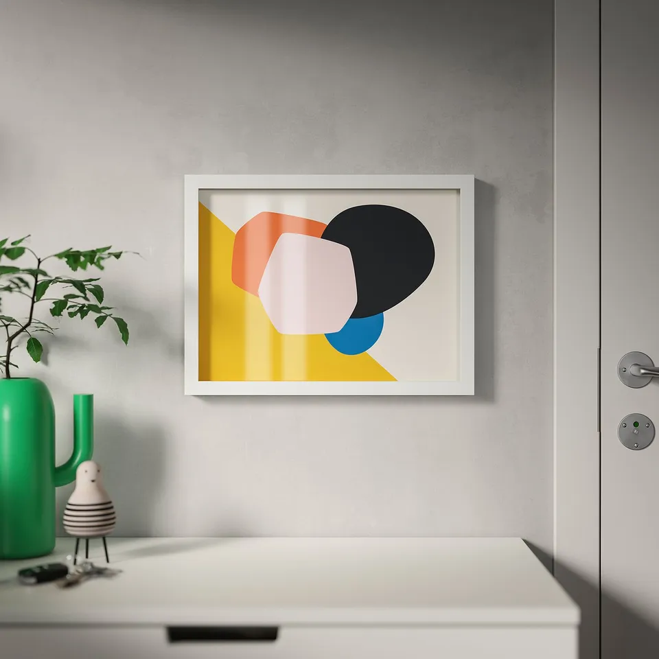 A white-framed picture on a wall near a cabinet, with colourful shapes on a beige/yellow background. A green vase with a plant sits on the cabinet.