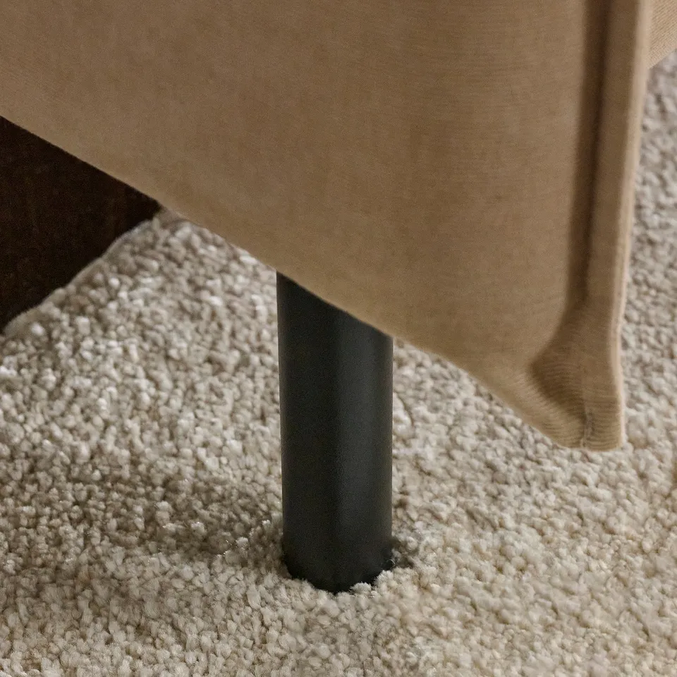 Modern sofa with tan upholstery, black metal legs on textured white carpet.