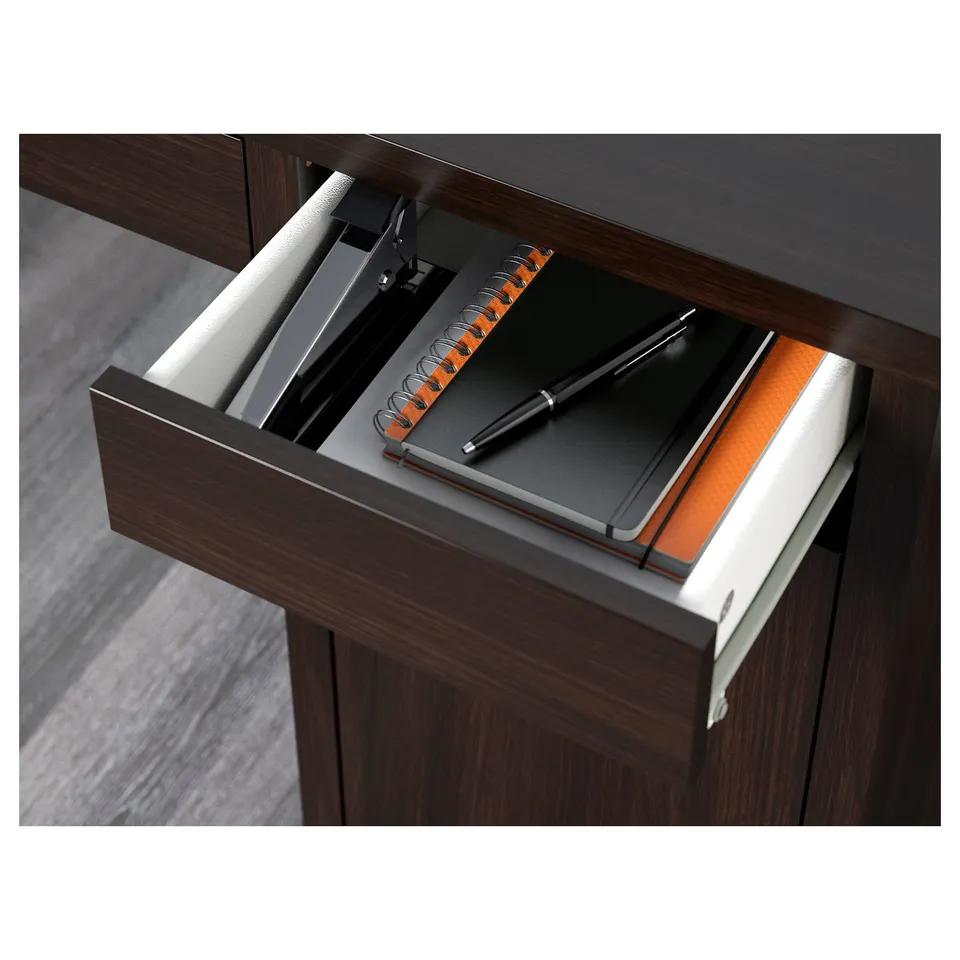 Open wooden desk drawer revealing a black notebook, pen, and binder clips organised within.