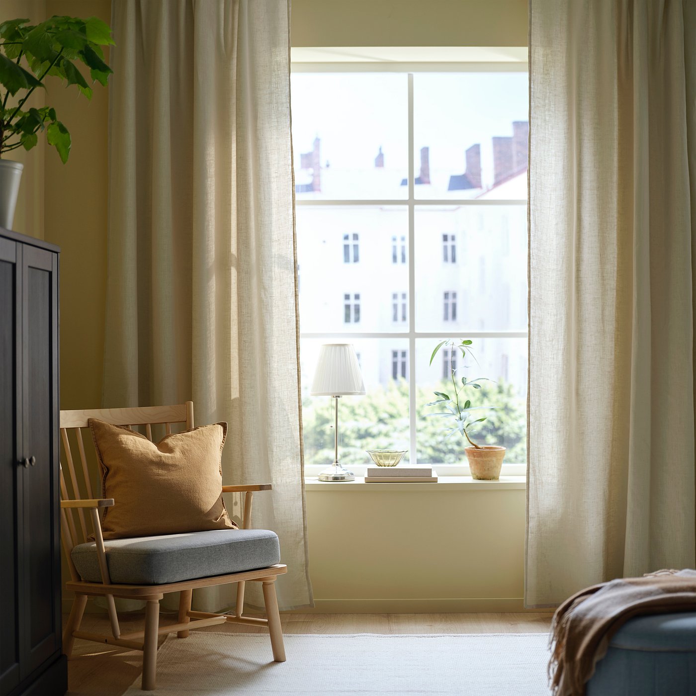 Bright room with large DYTÅG beige curtains, wooden chair, soft beige cushion, and potted plant on windowsill.
