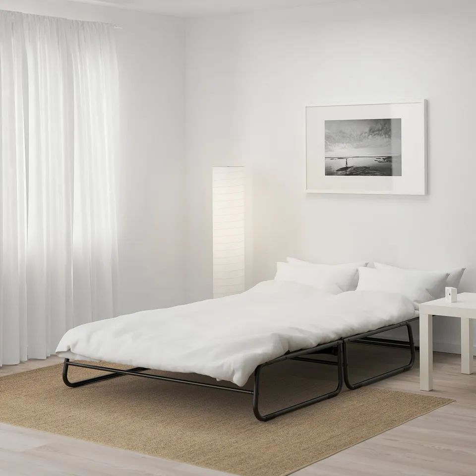 A modern bed in a minimalist room with white bedding, a side table, and a framed photo on the wall.