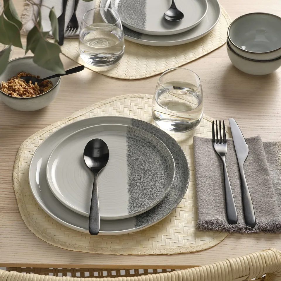 Table setting with grey, stoneware plates, modern design, metal cutlery, glasses on woven placemats.