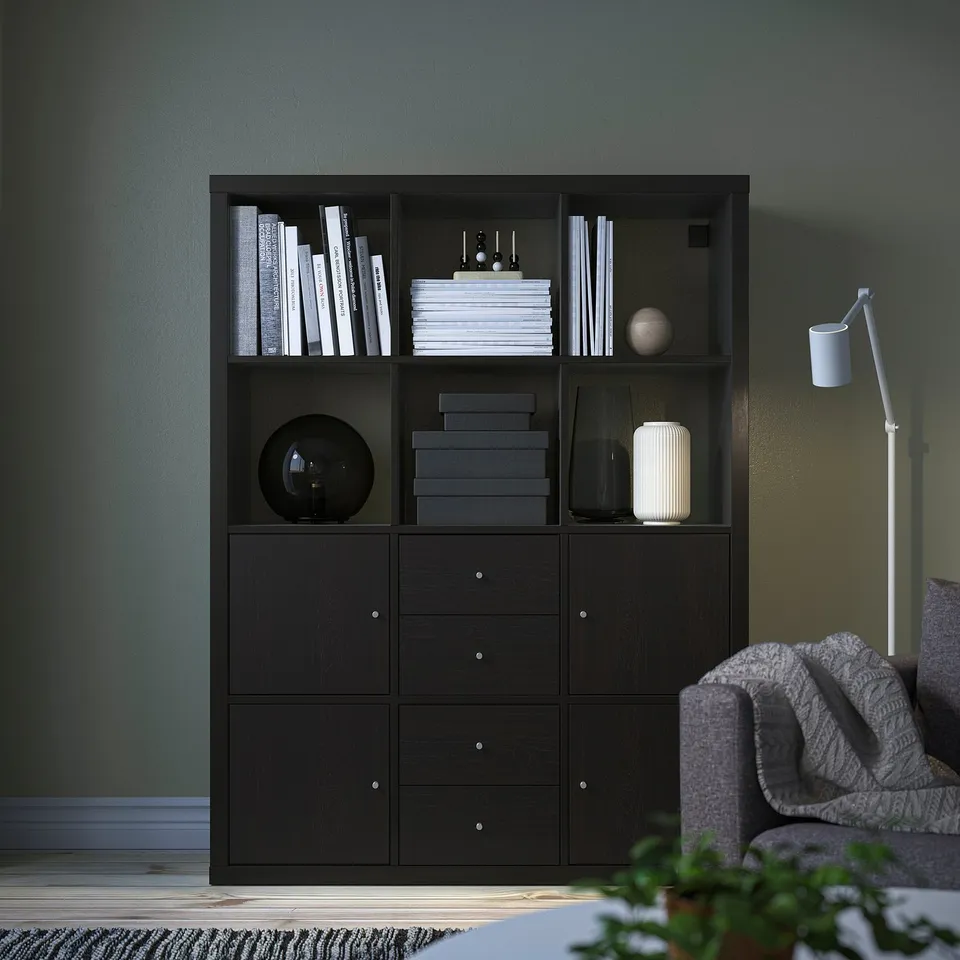 KALLAX black bookshelf with books & decor against green wall. Tall, rectangular, with storage.