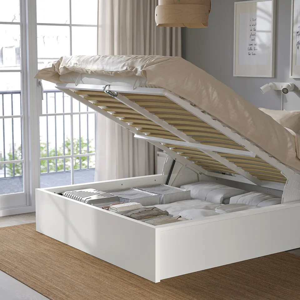 Bed with lift-up base reveals organised storage; white, slatted design; high headboard.