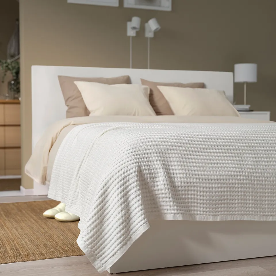 PELARTUJA bedspread on large bed, white waffle weave. Beige pillows, matching headboard, white lamp. Covers most of bed, slightly hanging over sides.