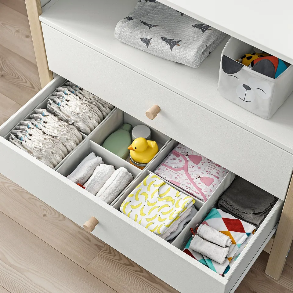 Organised changing table with open drawers, showing nappies, clothes, and a rubber duck. Part of the ÄLSKVÄRD series for baby care.