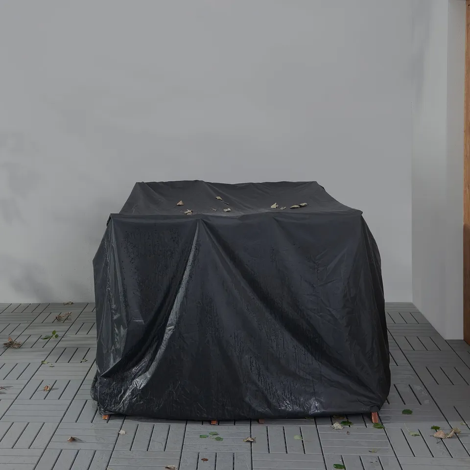 Black TOSTERÖ furniture cover, 4-seat, waterproof, outdoor, square shape, on wooden floor, against white wall.