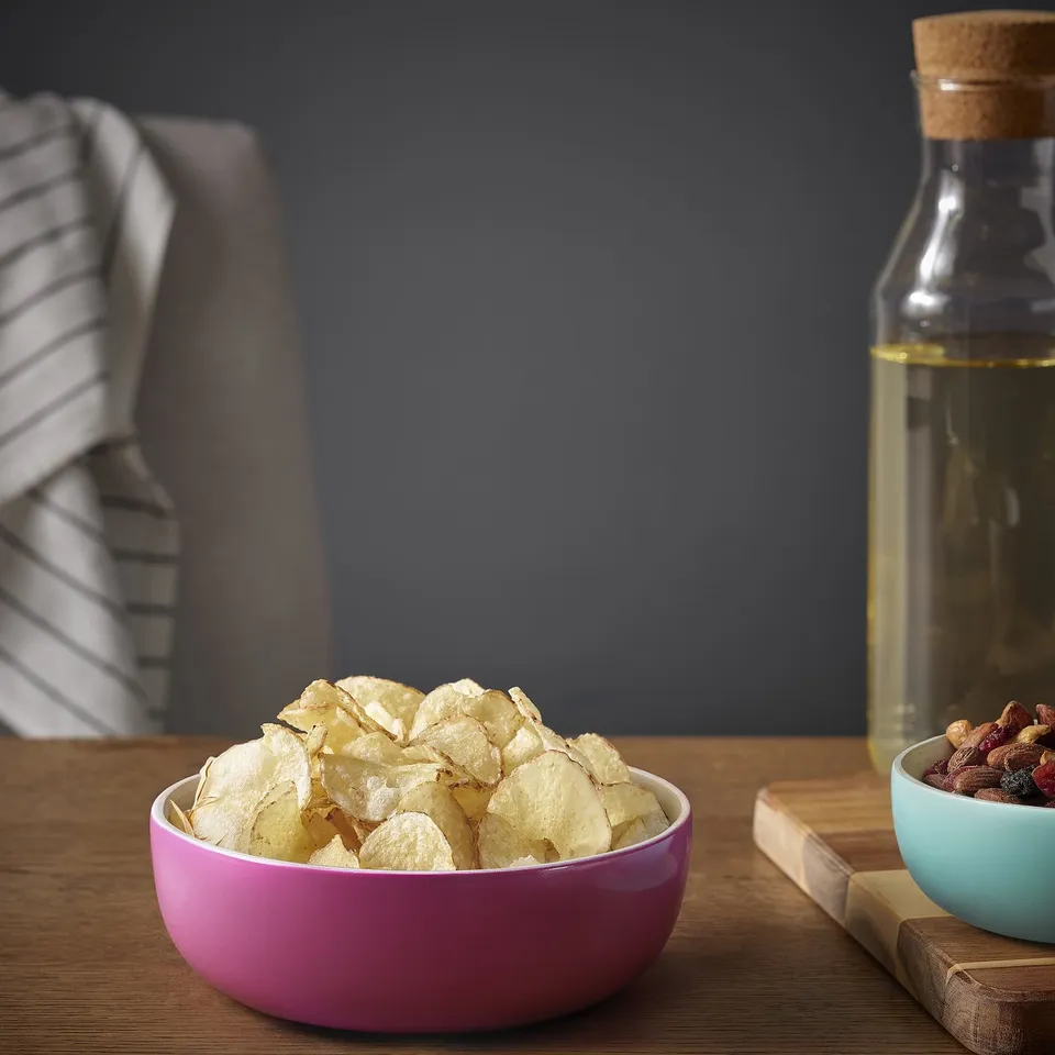 Magenta bowl of chips, oil jar, small blue nut bowl on wood table.
