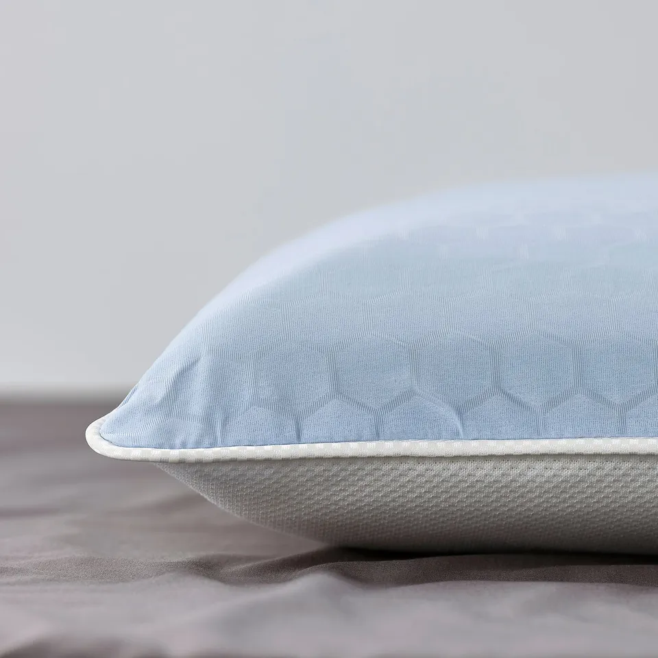 Blue ergonomic pillow featuring a textured honeycomb pattern, resting on a neatly made bed. High-quality, cool, and supportive.