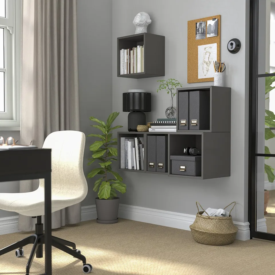 Black wall-mounted shelves store books & decor, with plant & chair below.