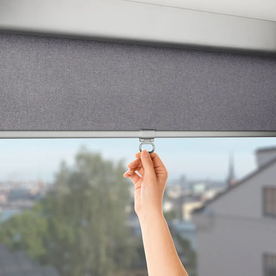 A hand pulls a TRETUR roller blind, showcasing its cordless, soft-closing feature, blocking out light.
