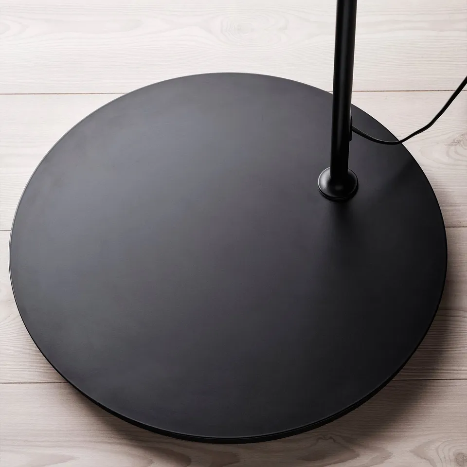 Large black circular floor lamp base on wooden floor.