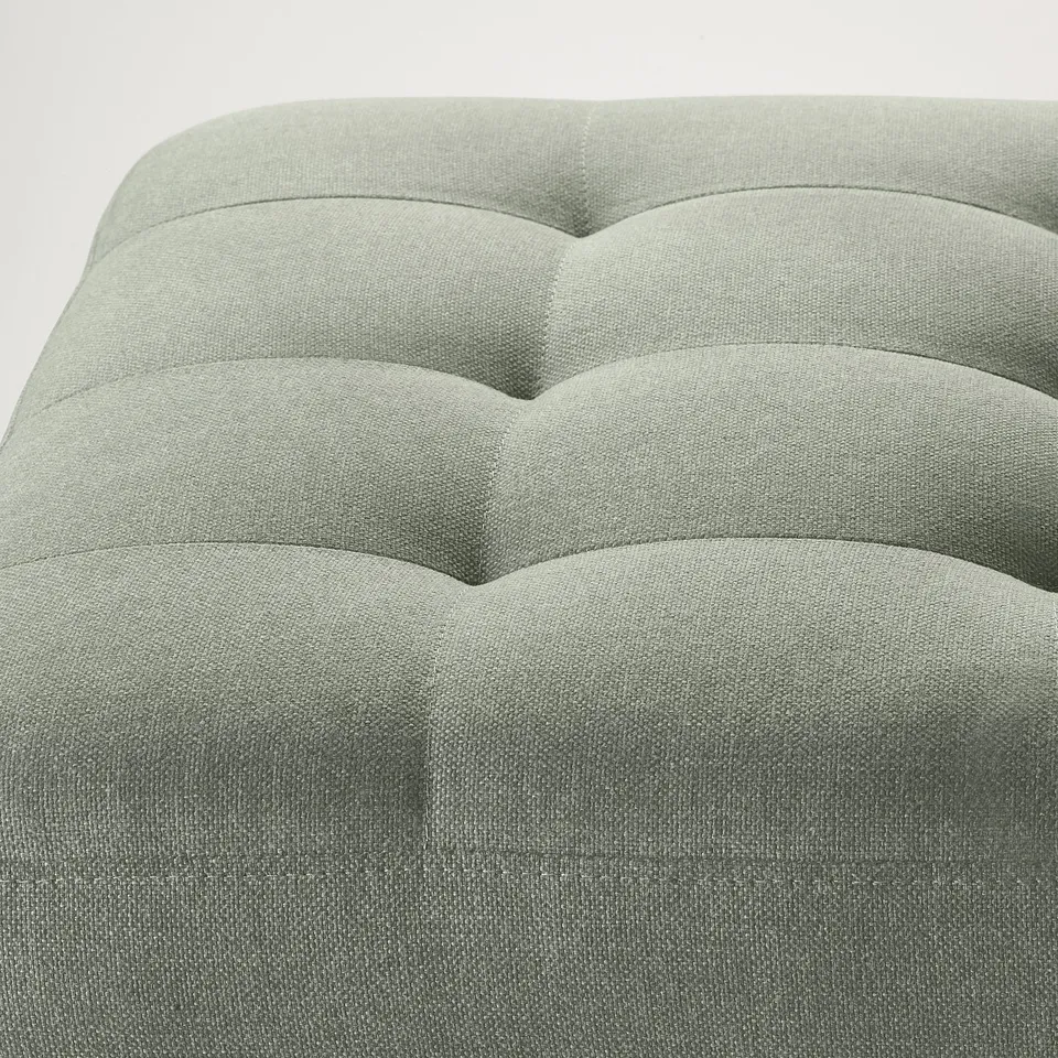 Modern footstool with wavy cushioned top, upholstered in soft grey fabric, designed for comfort and style.
