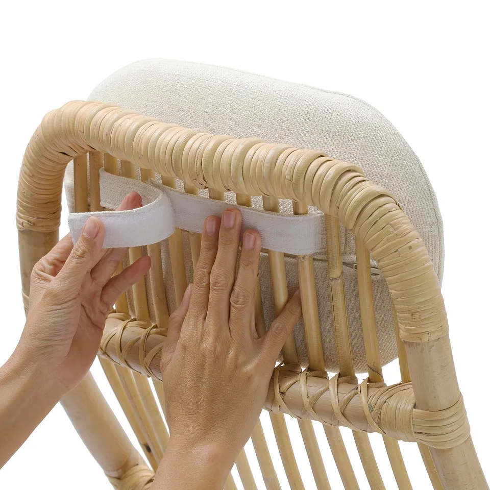 Hands attach a grey cushion to a wicker chair, securing with velcro for comfort and easy cleaning.