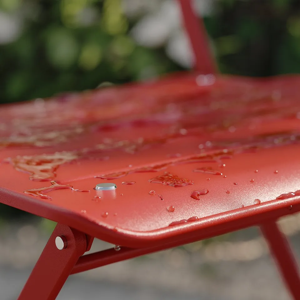 Bright red metal chair, wet with water droplets, outdoor setting.