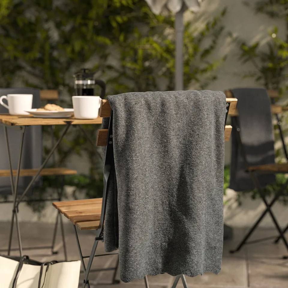 Dark grey fleece throw draped over chair, larger than coffee cups on table.