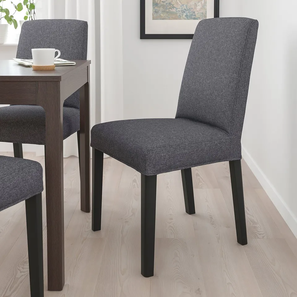 Modern grey BERGMUND chair with black legs, cushioned, ergonomic, next to dining table.