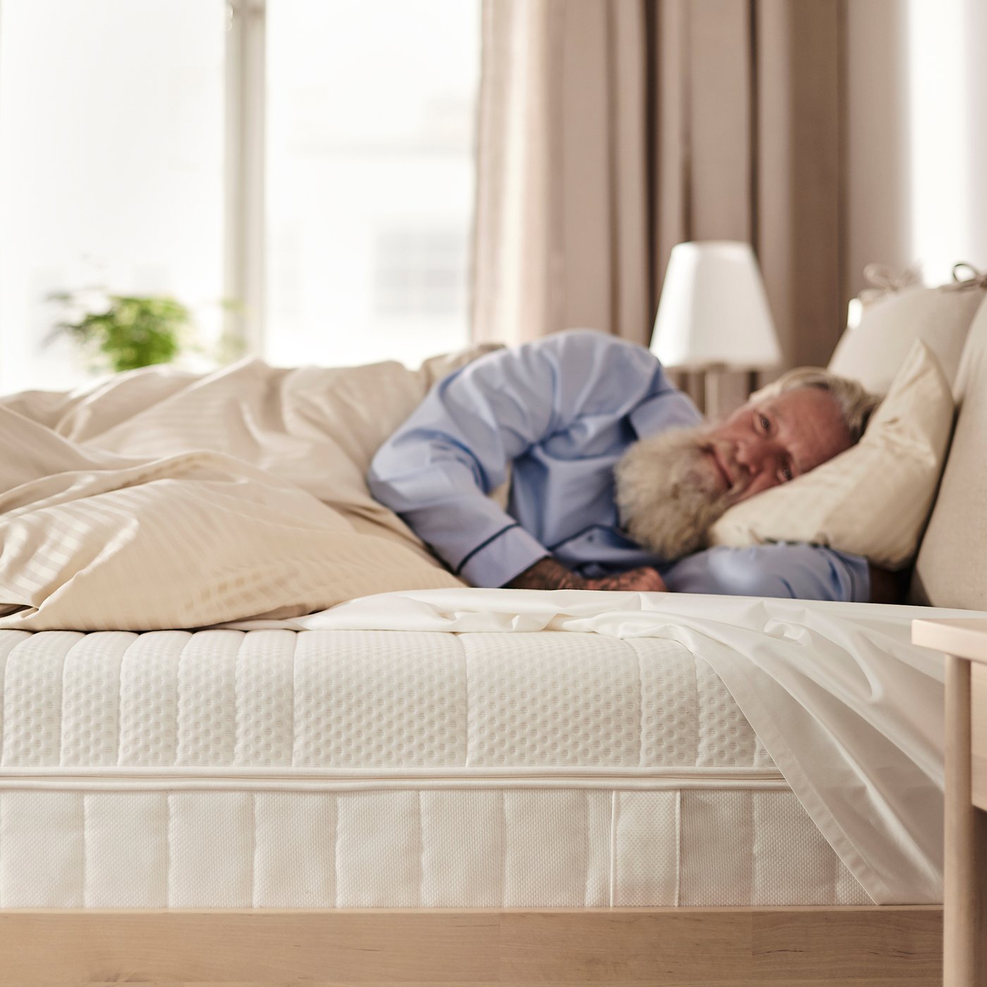 Comfortable bedroom scene with a person sleeping peaceful on a white ÅNNELAND hybrid mattress.