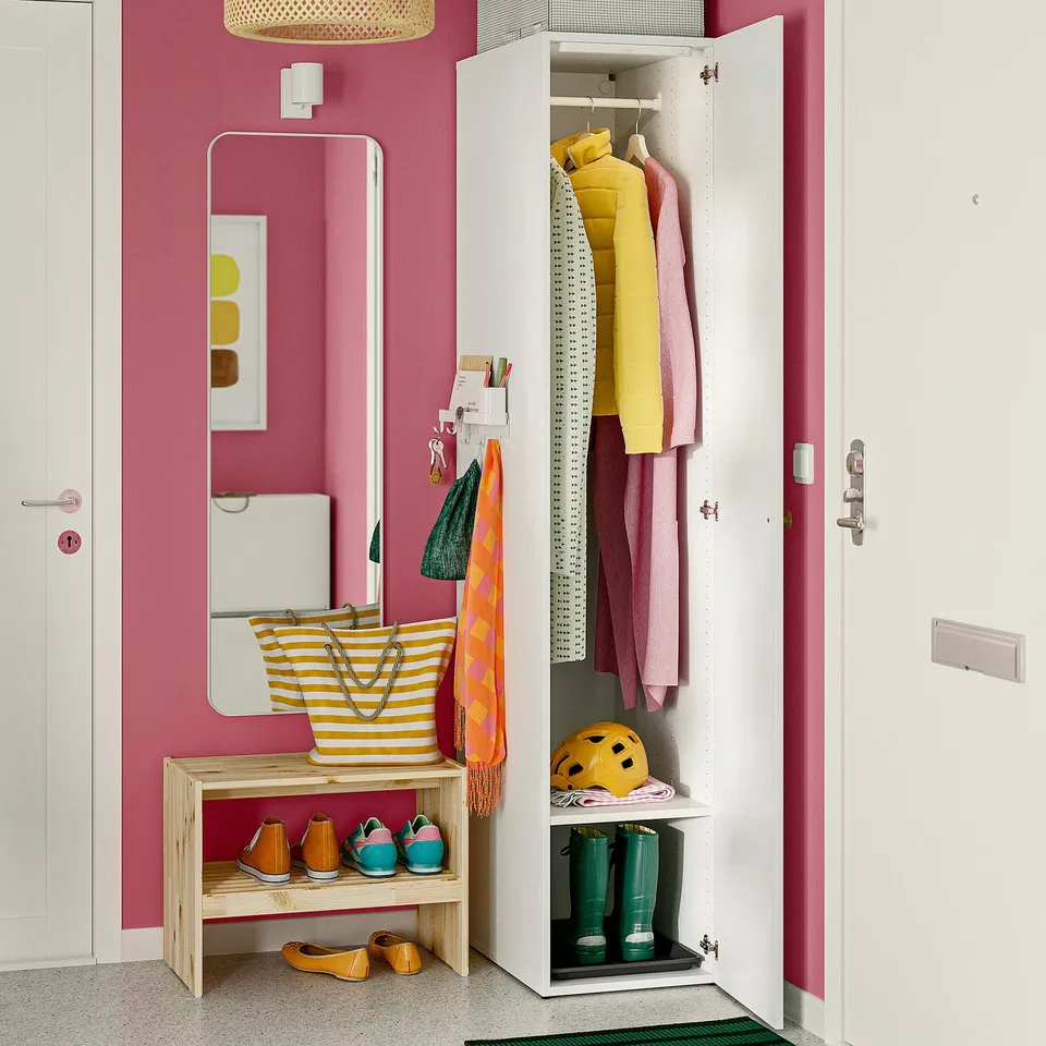 Colourful closet with hanging clothes, shoes, and organised accessories. Mirror, pink wall, and wooden bench create functional entryway.