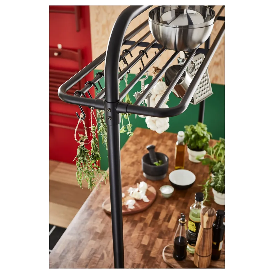 Black metal kitchen storage rack with hanging herbs and various kitchen tools.