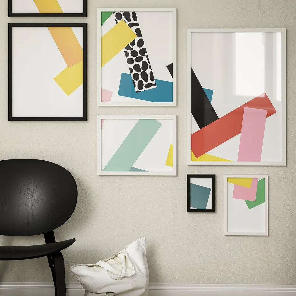 Six colourful abstract frames surround a black chair on a beige wall, with bright patterns and varying sizes.
