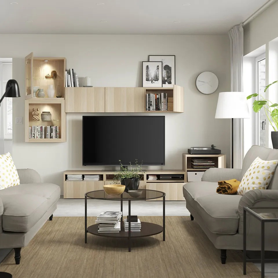 Modern living room with grey couches, wooden tv stand, and shelves. Flat-screen tv, books, decor, and a plant on coffee table.