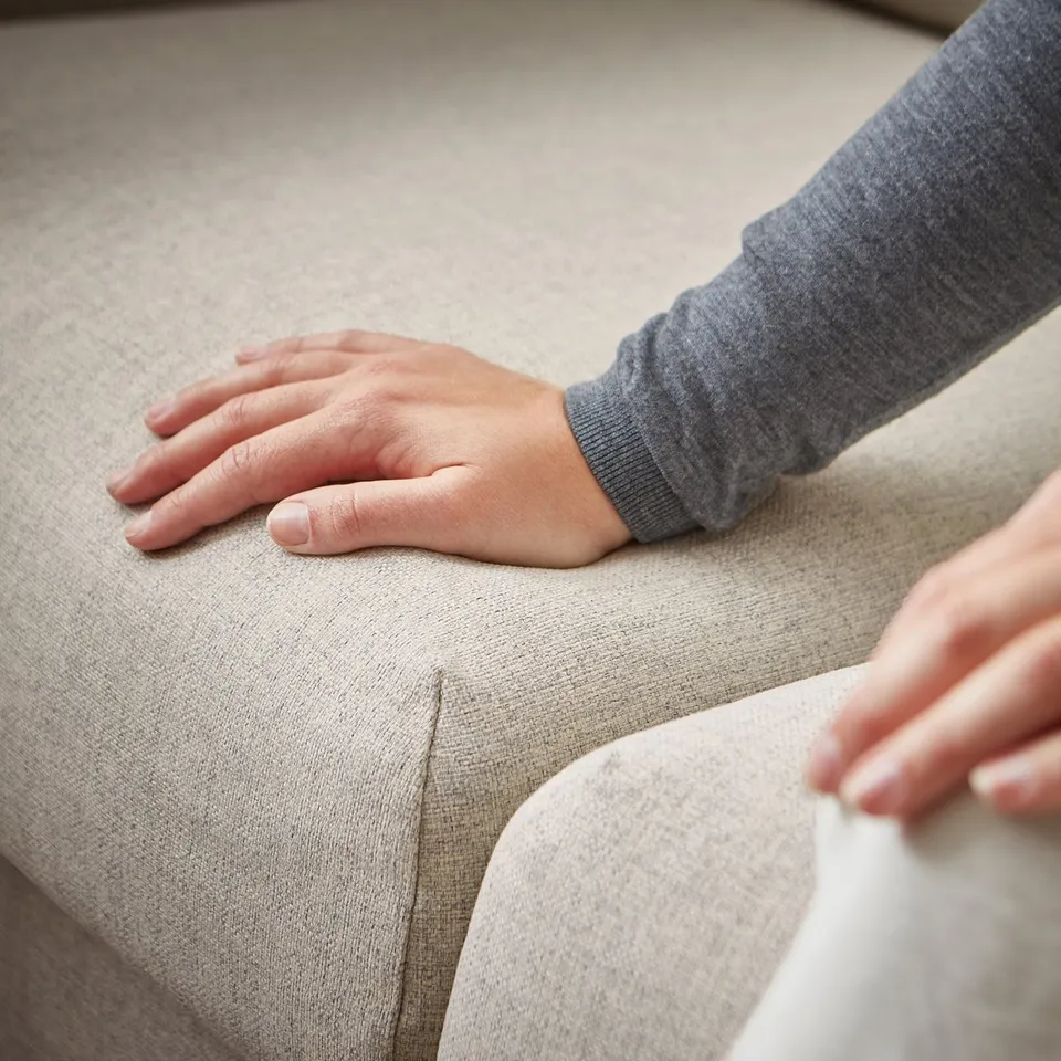 Hands testing the comfort of a beige VIMLE sofa.