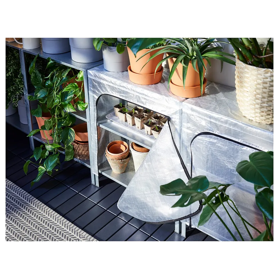 Small greenhouse setup on a grey deck. Includes a grey metal shelf and various potted plants in clay and wicker pots.