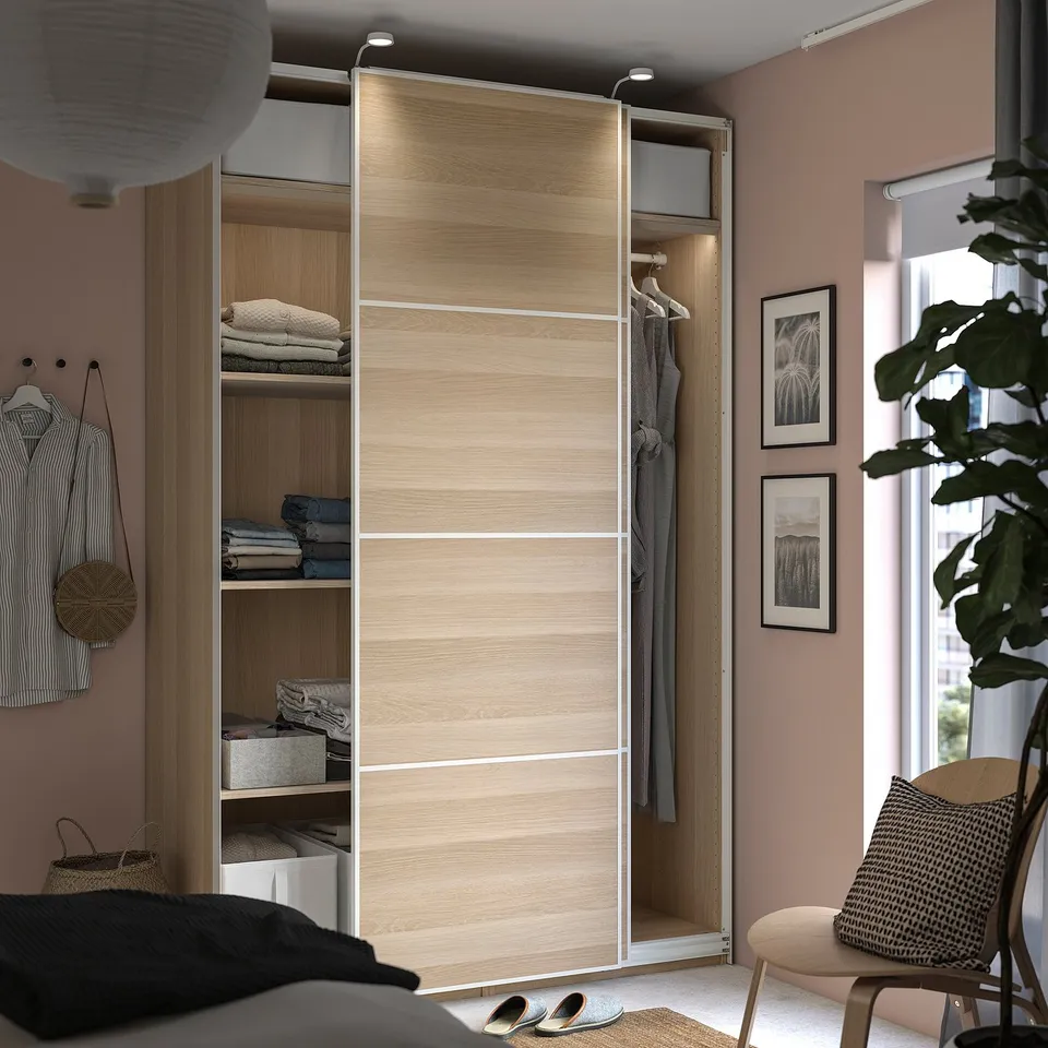 Modern bedroom with light wood PAX wardrobe, shelves, hangers, and sliding door.