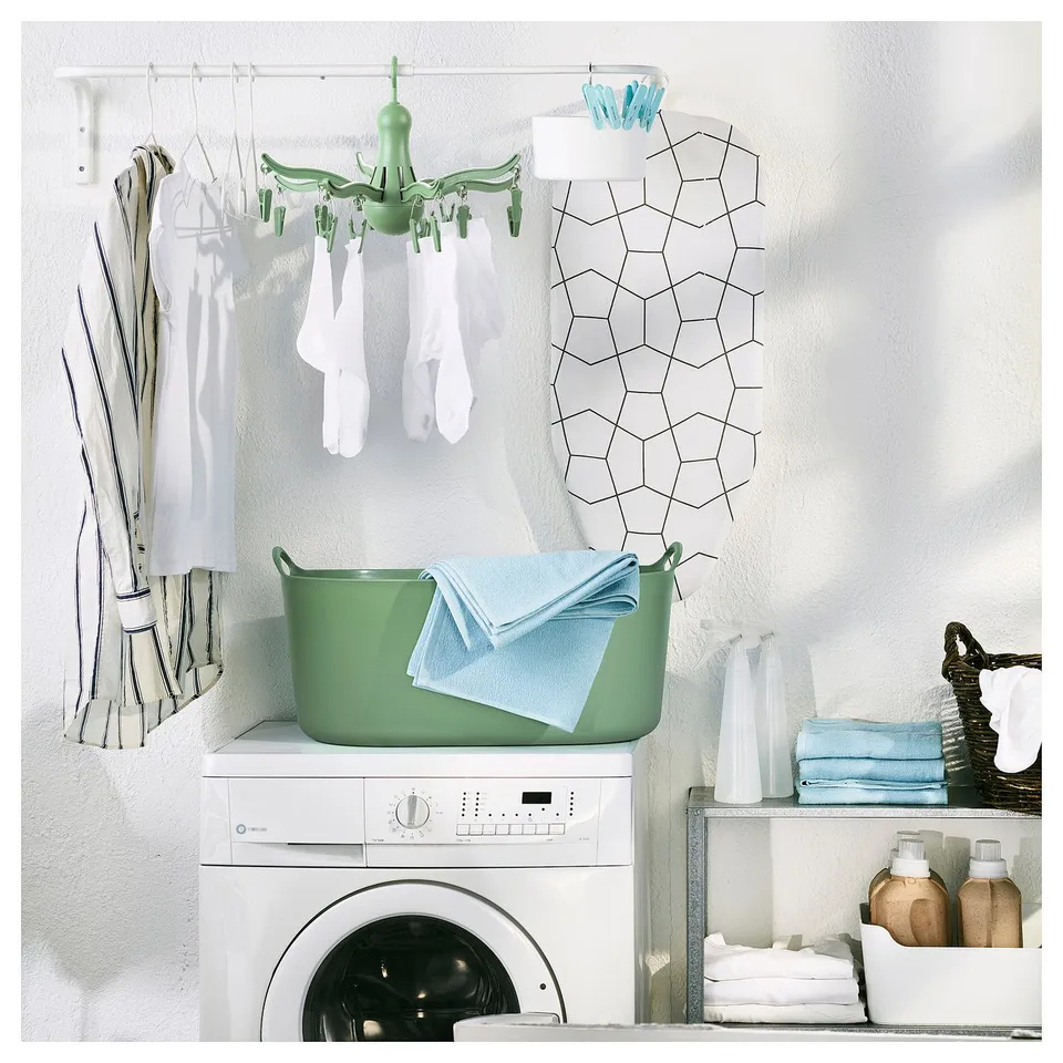 Small, green, plastic indoor/outdoor laundry dryer with 16 pegs, hanging socks and underwear, placed on a white washing machine.