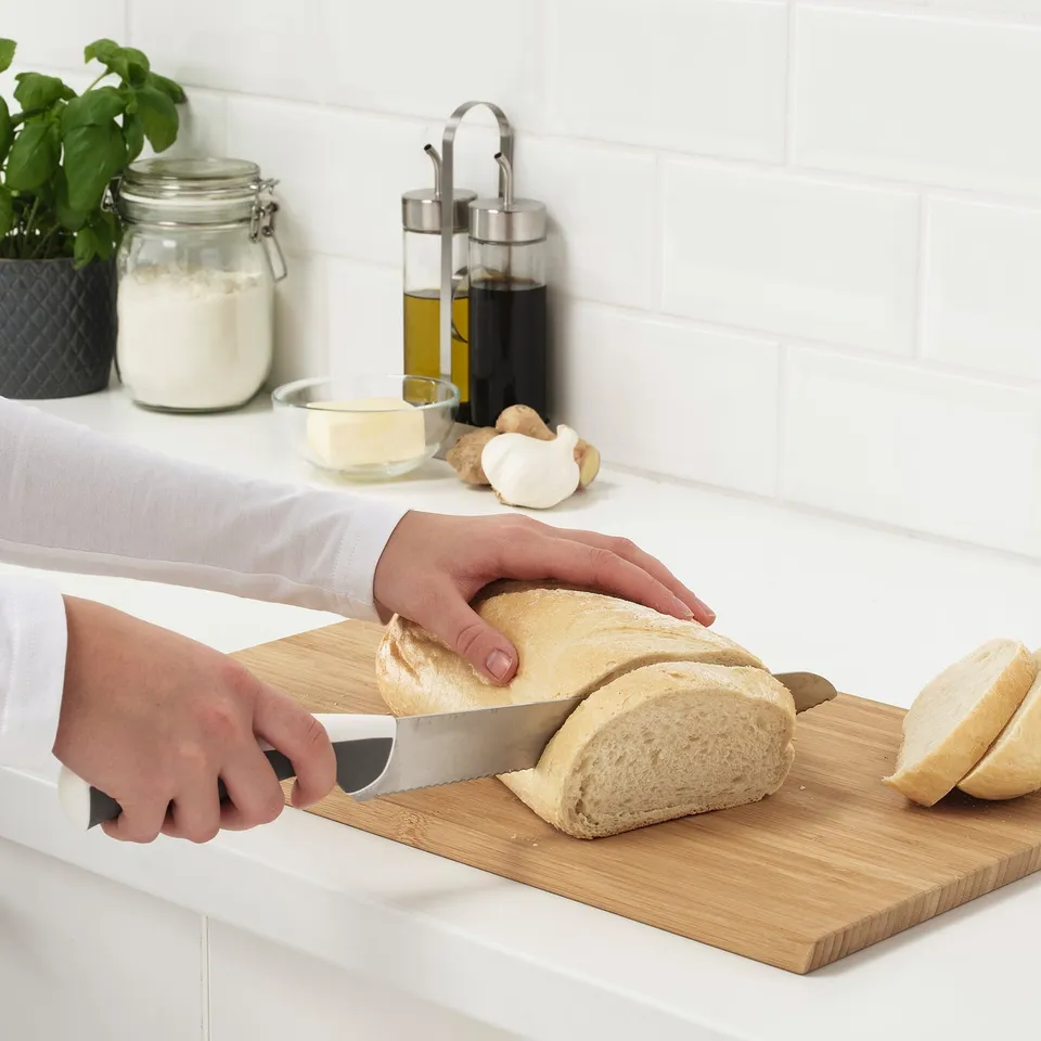 Person slices bread on wooden cutting board with knife in kitchen.