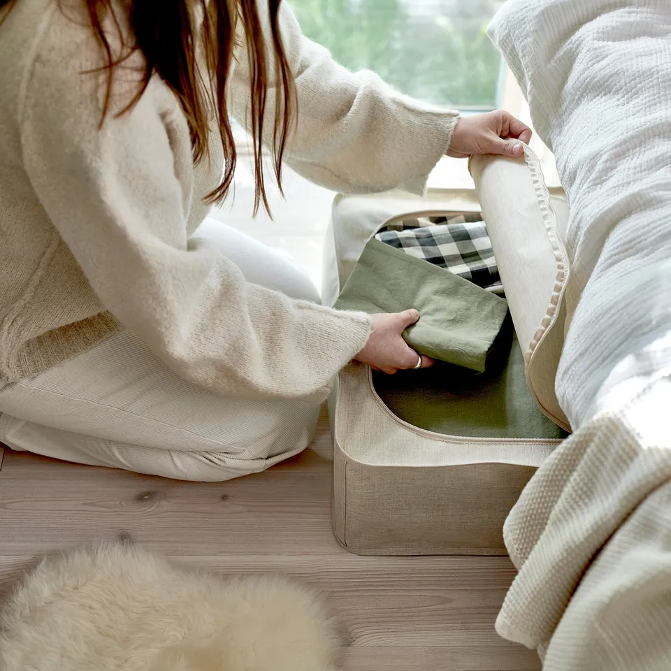 Person placing a fabric storage case with handles under a bed. The case has ventilation holes and fits well under the bed.