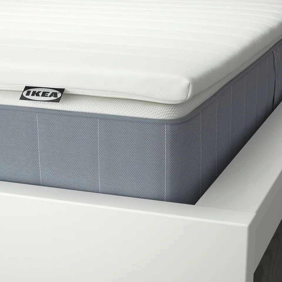 Close-up of IKEA mattress with padded top, edge stitching visible, on a white bed frame.