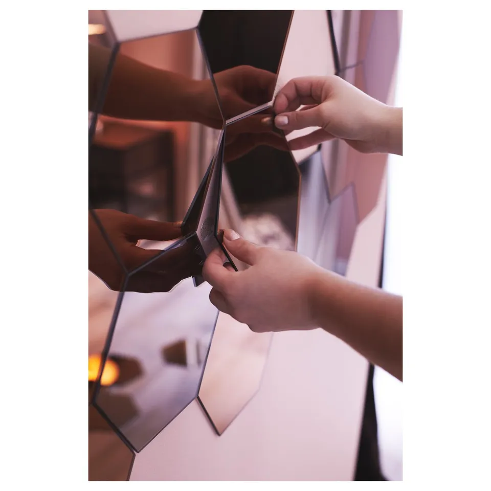 Hands assemble geometric mirrors with reflective surfaces and brown-tinted glass.
