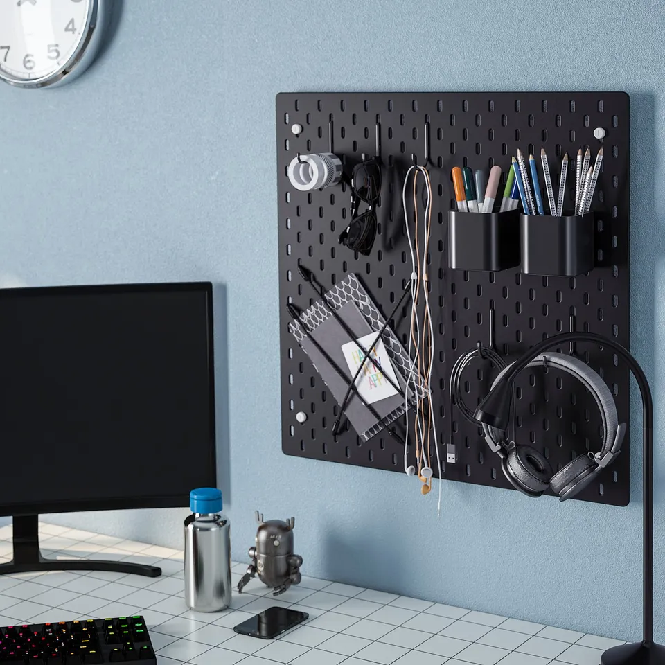 Wall-mounted black pegboard with hooks holding headphones, pens, and cables. Below, a desk with a monitor, keyboard, and other items.