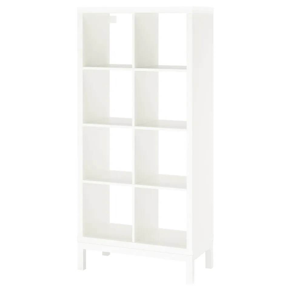 A white KALLAX shelving unit. It has a modern, cube-shaped design with multiple open shelves supported by a metal underframe.