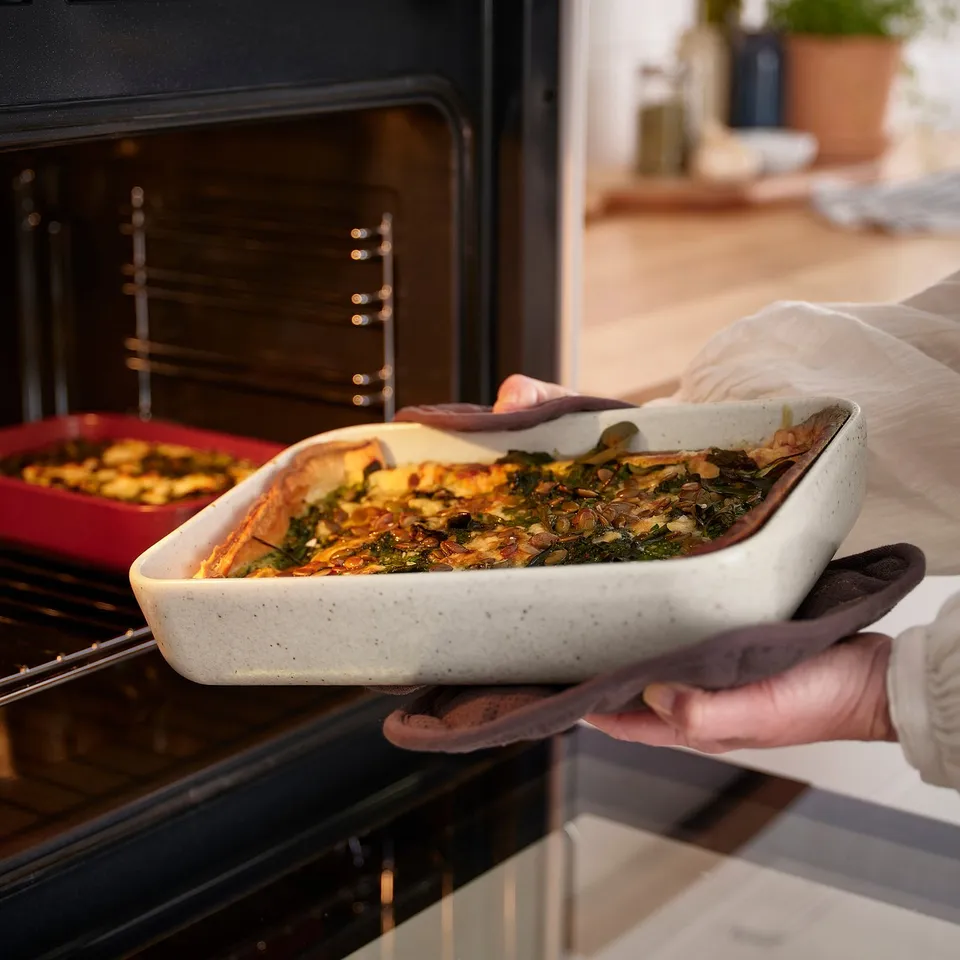 Person placing baked dish into oven, with another dish inside. Suitable for small meals or gatherings.