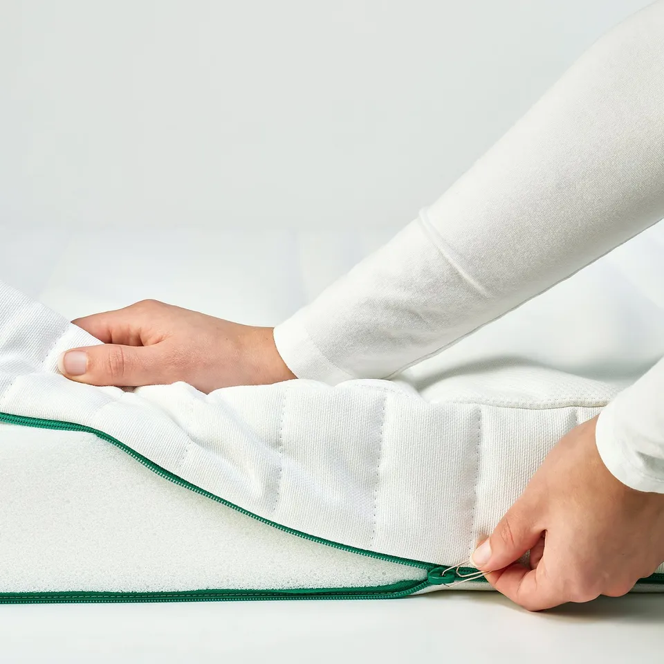 A person zips a white mattress cover, showcasing its easy-to-use child-safe zip.