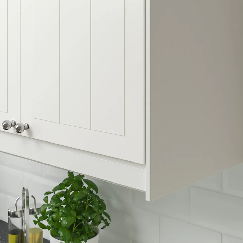 Kitchen with white grooved cabinets. Green plant on counter, silvery handles.