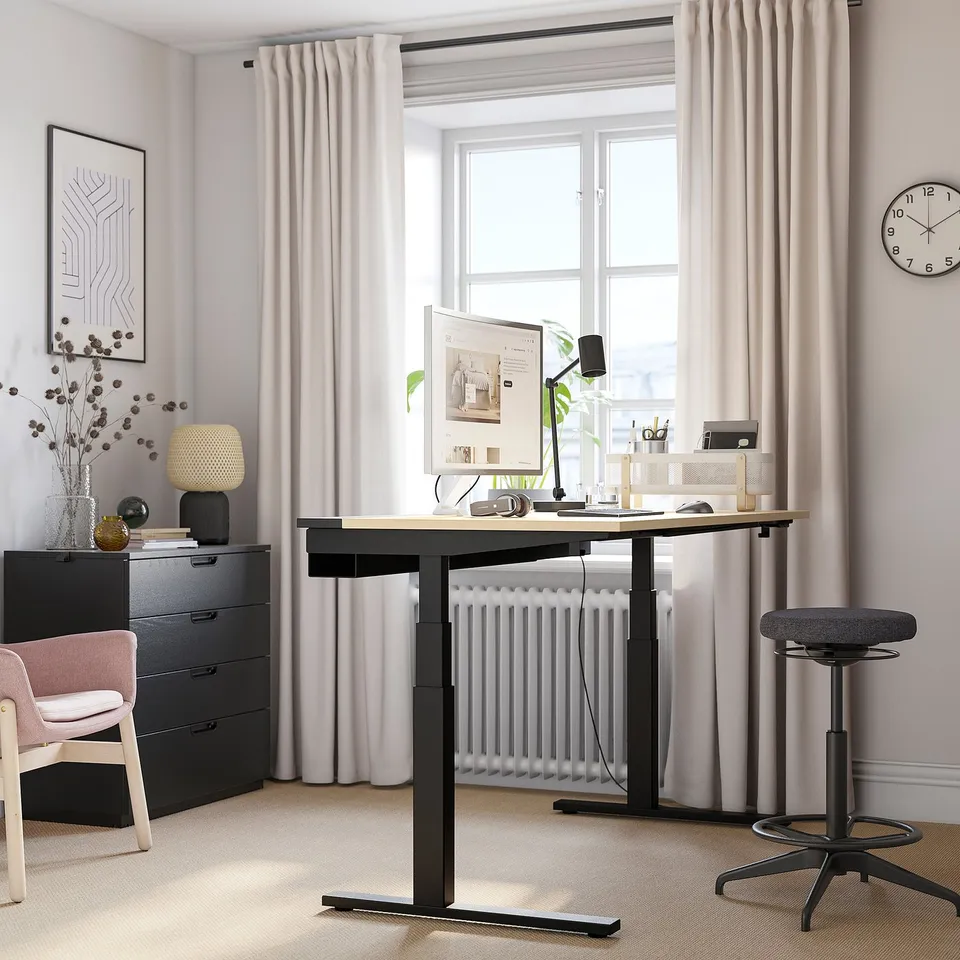 Modern home office setup featuring MITTZON black sit/stand desk by large window, black chair, white radiator, and blush curtains.
