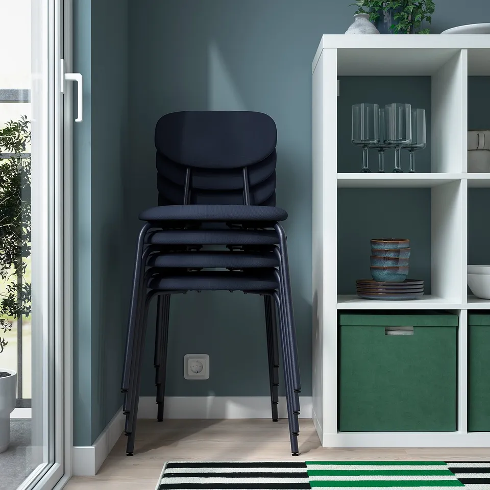 Stacked upholstered chairs against a wall. The chairs feature metal underframes and are designed for indoor use.