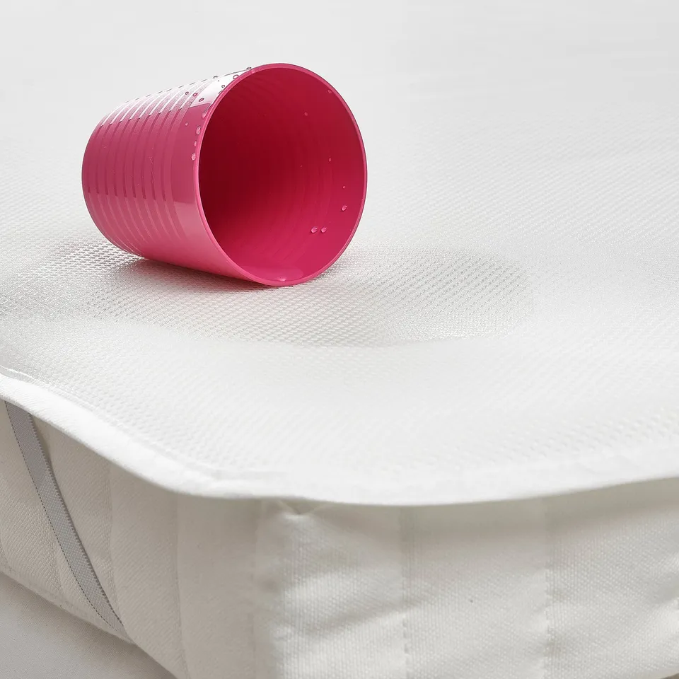 Pink cup on white mattress protector, designed to catch spills.