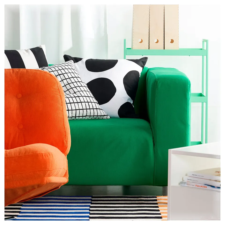 Vibrant living room with bright orange chair, green sofa, and white pillow with black dots on a colourful striped rug.
