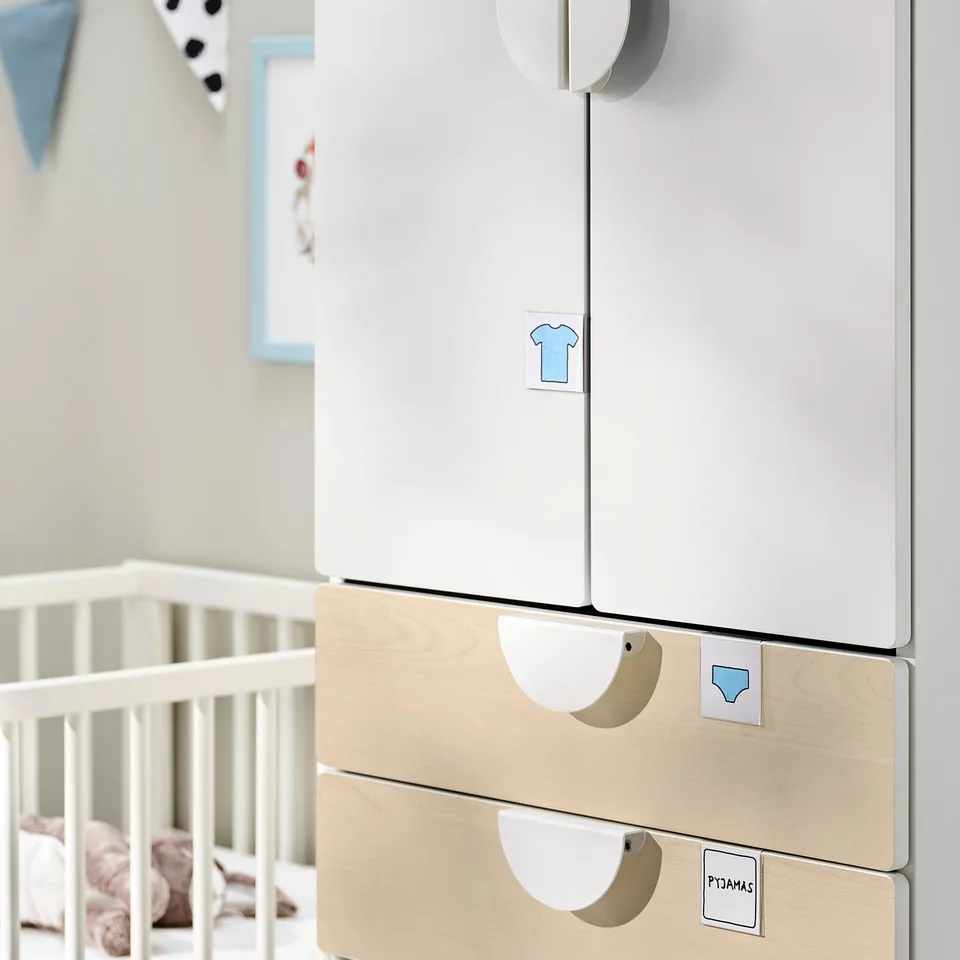Modern nursery wardrobe with light wood drawers, white doors, and soft-close hinges, located near a white crib.