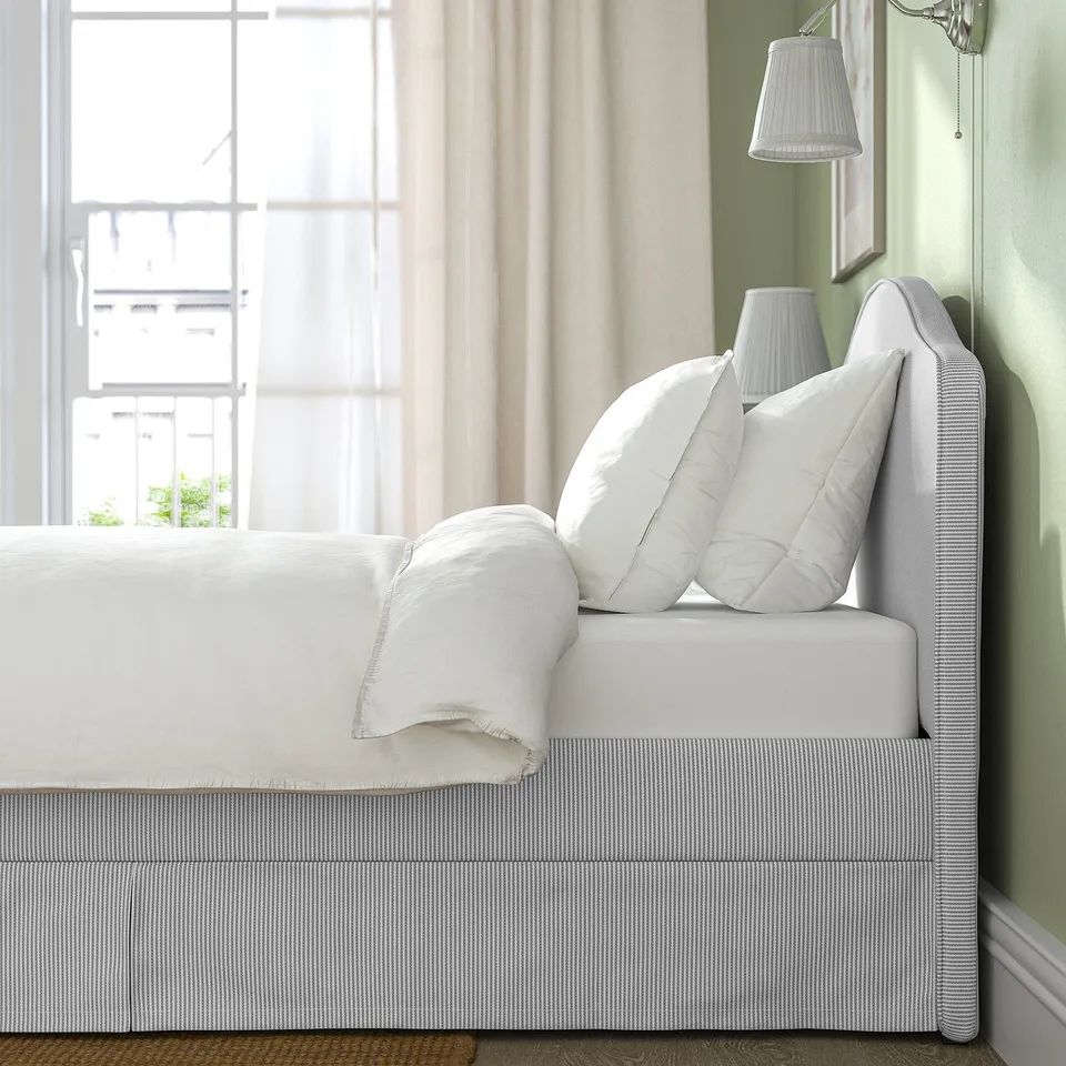 Cosy bed with curved headboard, white pillows, and striped bedding near large window with sheer curtains.