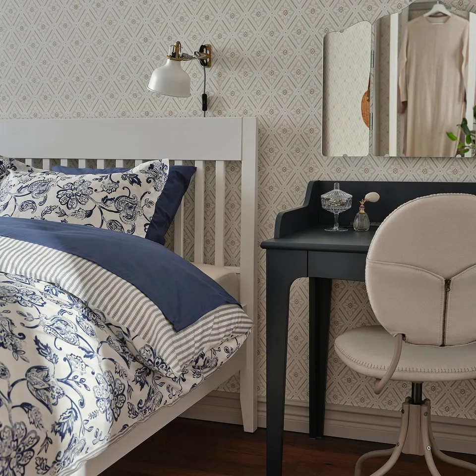 Elegant bedroom with white IDANÄS bed, blue floral linens, wooden vanity, and mirror.